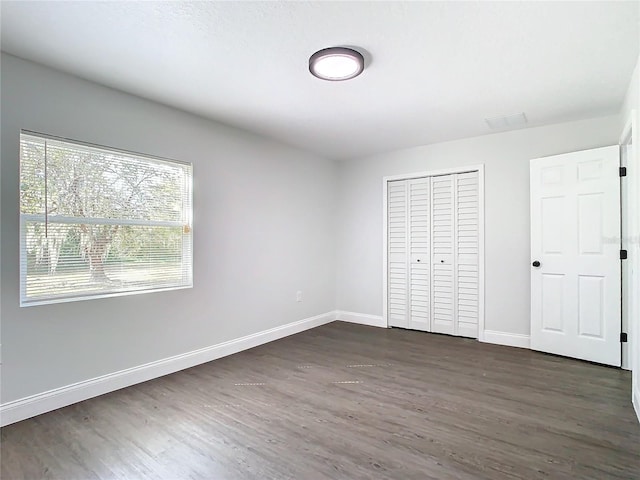 unfurnished bedroom featuring dark wood-style floors, baseboards, and a closet