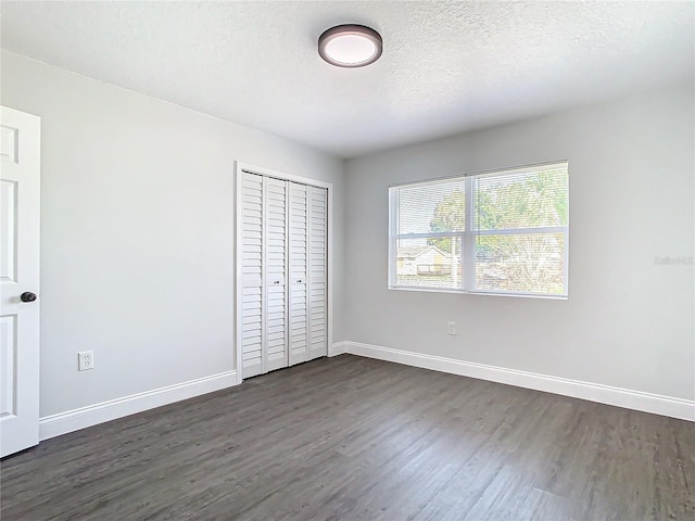 unfurnished bedroom featuring a closet, dark wood-style flooring, a textured ceiling, and baseboards