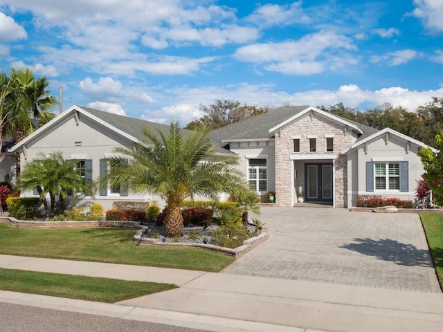 view of front facade with stone siding, french doors, driveway, stucco siding, and a front yard