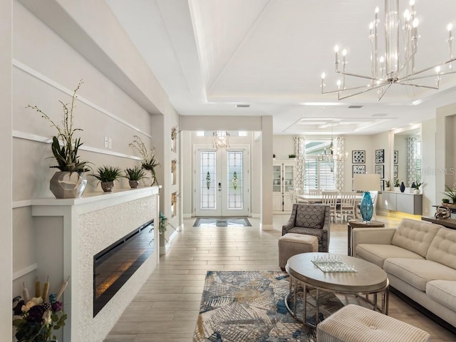 living room with a notable chandelier, a glass covered fireplace, wood finished floors, french doors, and a raised ceiling