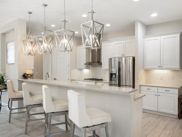 kitchen with stainless steel appliances, white cabinetry, a kitchen breakfast bar, light countertops, and wall chimney exhaust hood