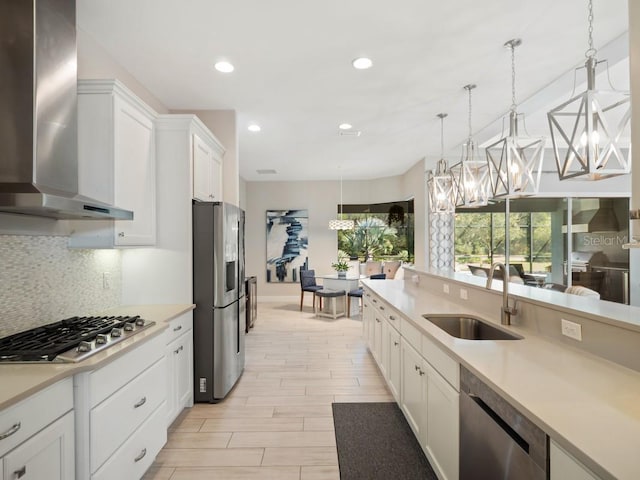 kitchen featuring tasteful backsplash, appliances with stainless steel finishes, white cabinets, a sink, and wall chimney range hood