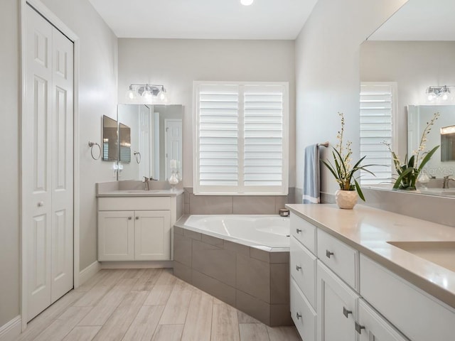 bathroom featuring two vanities, plenty of natural light, a garden tub, and a sink