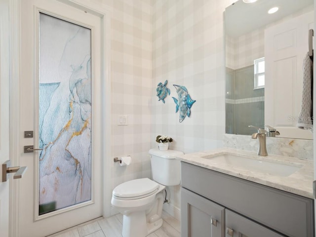 bathroom with vanity, toilet, and wallpapered walls