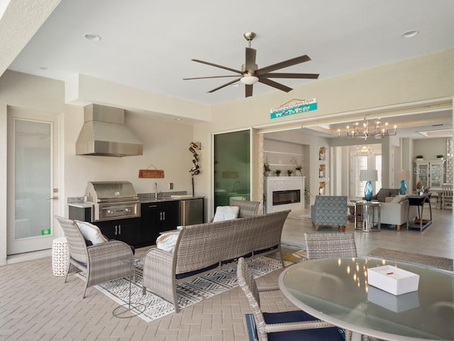 living room with brick floor, a glass covered fireplace, and ceiling fan with notable chandelier