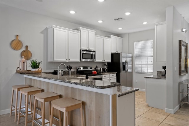 kitchen featuring dark stone counters, a peninsula, appliances with stainless steel finishes, and light tile patterned floors