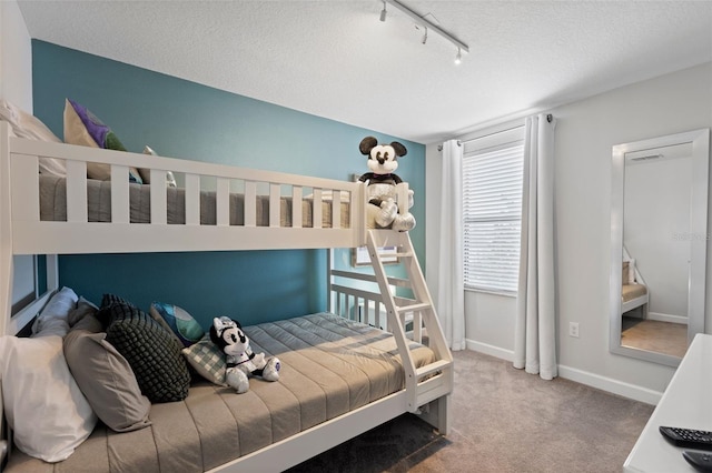 carpeted bedroom featuring rail lighting, a textured ceiling, and baseboards