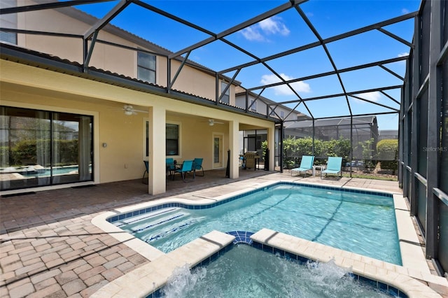 view of swimming pool with glass enclosure, a pool with connected hot tub, a ceiling fan, and a patio