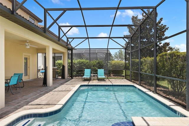 outdoor pool with a patio, glass enclosure, and a ceiling fan