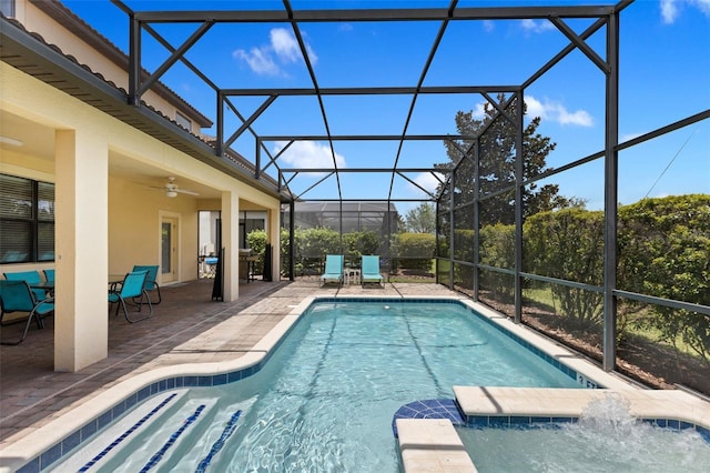 view of swimming pool featuring glass enclosure, a pool with connected hot tub, a patio area, and a ceiling fan