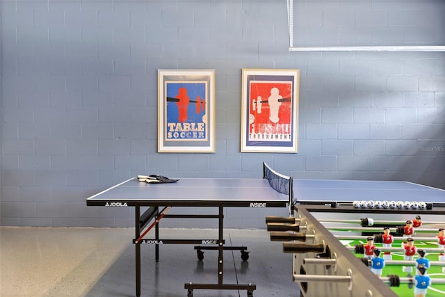 game room with concrete block wall and finished concrete flooring