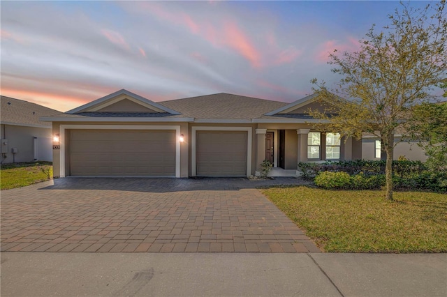 view of front of property featuring decorative driveway, a yard, stucco siding, a shingled roof, and a garage