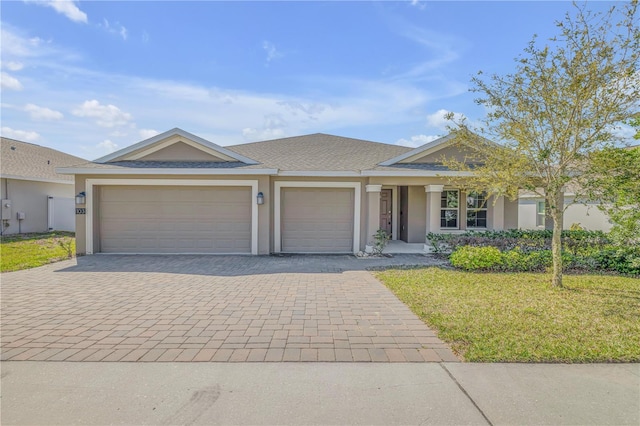 ranch-style home featuring a front lawn, decorative driveway, an attached garage, and stucco siding