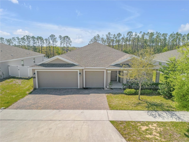 view of front of property featuring decorative driveway, stucco siding, a front yard, fence, and a garage