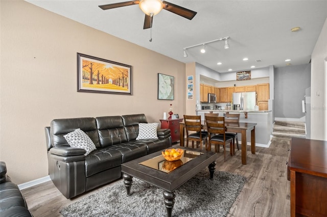 living area featuring light wood finished floors, rail lighting, a ceiling fan, and baseboards