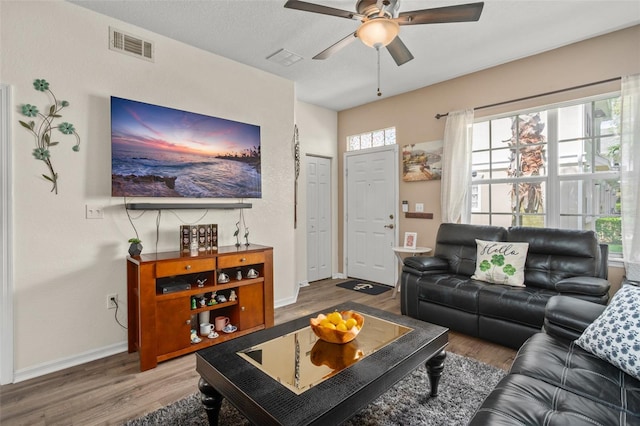 living room with baseboards, visible vents, a ceiling fan, wood finished floors, and a textured ceiling