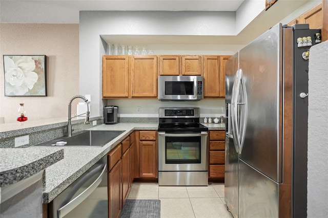 kitchen featuring stainless steel appliances, light tile patterned flooring, a sink, and brown cabinets