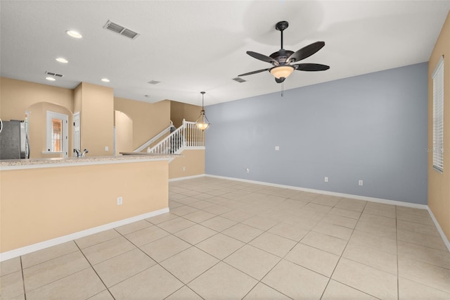 empty room featuring arched walkways, visible vents, a ceiling fan, baseboards, and stairs