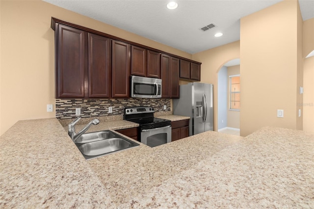 kitchen featuring visible vents, decorative backsplash, appliances with stainless steel finishes, dark brown cabinetry, and a sink