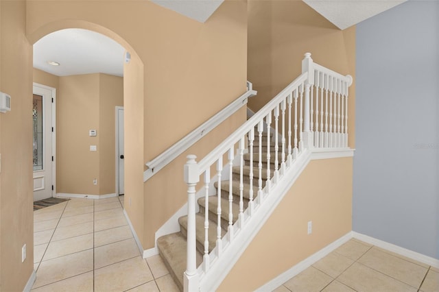 stairway featuring arched walkways, tile patterned flooring, and baseboards