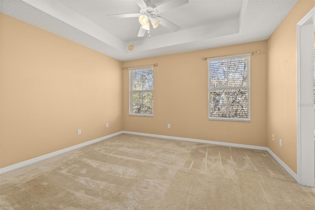 carpeted empty room with a ceiling fan, a tray ceiling, and baseboards