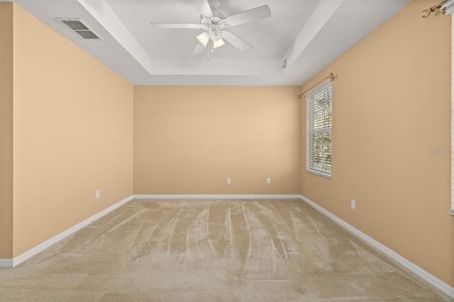 unfurnished room featuring a tray ceiling, light colored carpet, visible vents, ceiling fan, and baseboards