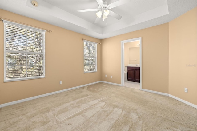 unfurnished room with light carpet, baseboards, a tray ceiling, and a ceiling fan