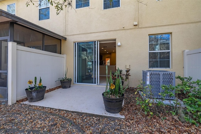 doorway to property with central AC unit, stucco siding, fence, and a patio