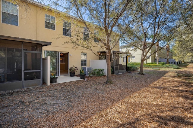 back of house with a sunroom, central AC, and stucco siding