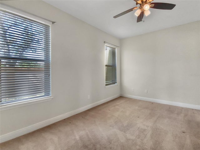 spare room with ceiling fan, baseboards, a wealth of natural light, and light colored carpet