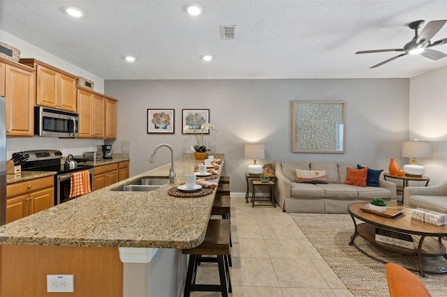 kitchen with visible vents, appliances with stainless steel finishes, open floor plan, a sink, and a kitchen bar