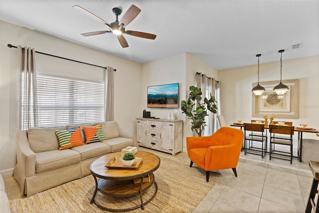 living area featuring light tile patterned floors, ceiling fan, visible vents, and a textured ceiling