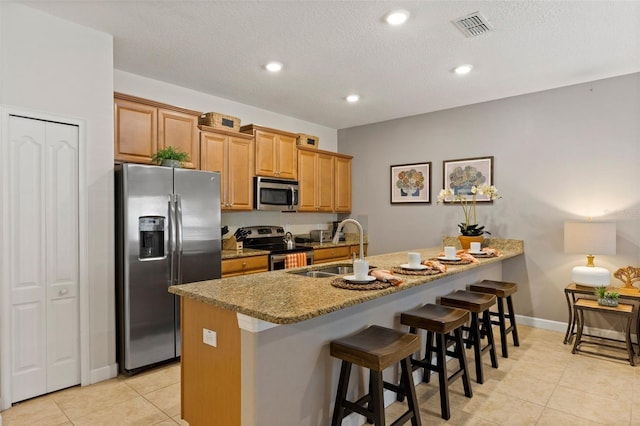 kitchen with a breakfast bar, stainless steel appliances, visible vents, a sink, and light stone countertops