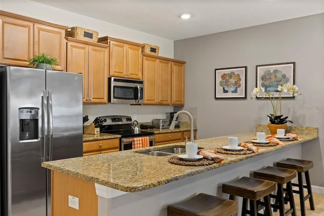 kitchen with light stone counters, stainless steel appliances, a kitchen bar, a sink, and baseboards