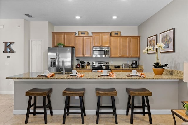 kitchen featuring stainless steel appliances, a breakfast bar, visible vents, and light stone counters