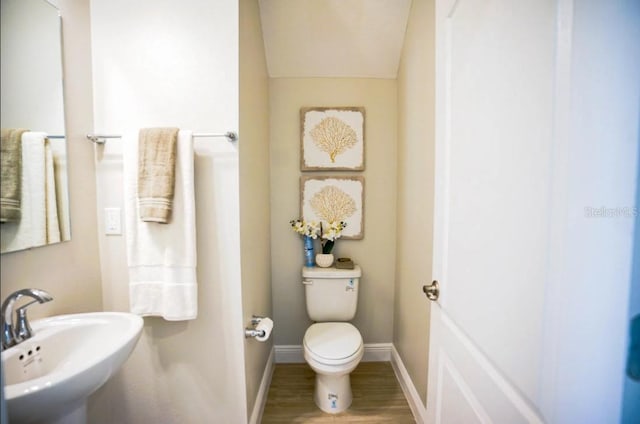 half bathroom featuring wood finished floors, a sink, toilet, and baseboards