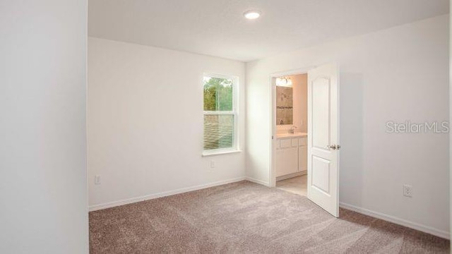 unfurnished bedroom with light carpet, connected bathroom, and baseboards