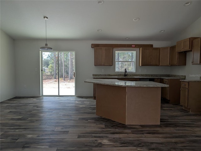 kitchen with light stone counters, a sink, a kitchen island, dark wood-style floors, and pendant lighting