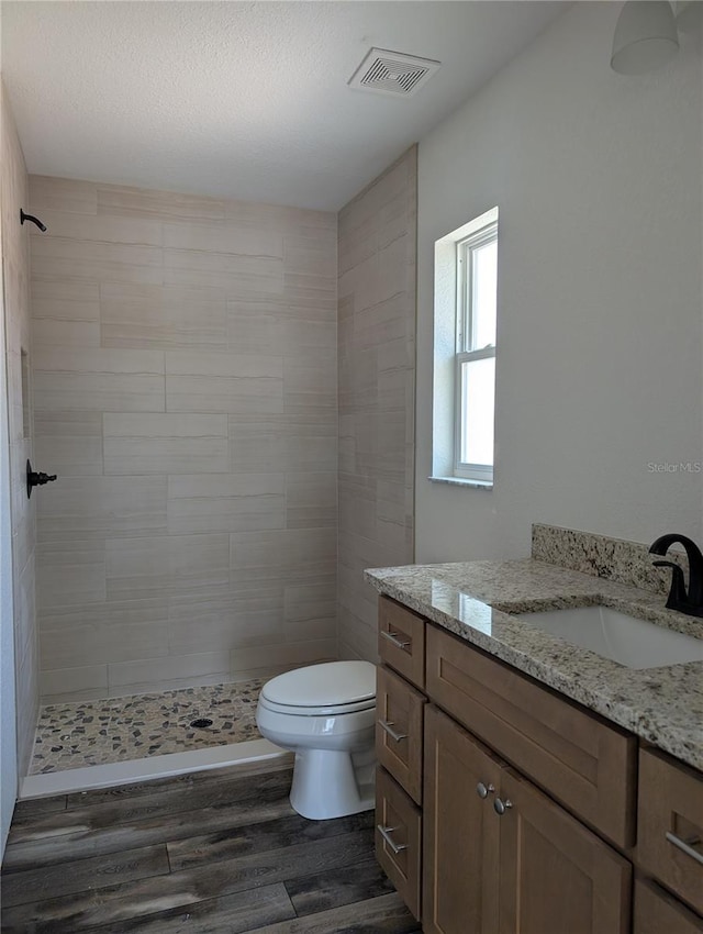 full bath with visible vents, toilet, wood finished floors, a tile shower, and vanity