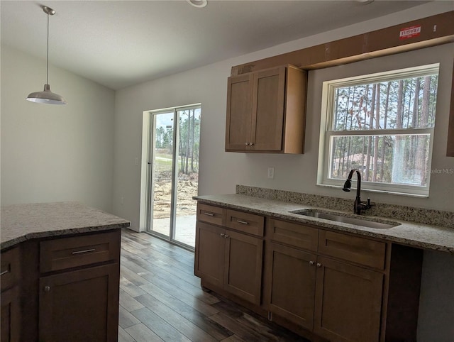 kitchen featuring hanging light fixtures, a sink, light wood-style flooring, and light stone countertops