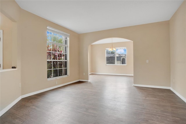 unfurnished room with arched walkways, baseboards, an inviting chandelier, and wood finished floors