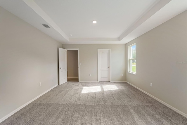 unfurnished room with recessed lighting, light carpet, visible vents, baseboards, and a raised ceiling