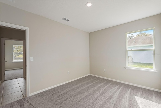 unfurnished room featuring light tile patterned floors, baseboards, visible vents, and light colored carpet