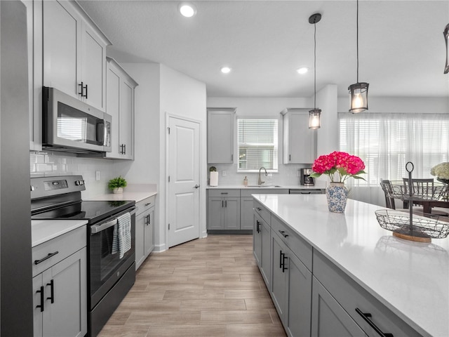 9747 Petition Way, Orlando, FL 32832 - kitchen with gray cabinets, light countertops, stainless steel appliances, a sink, and hanging light fixtures