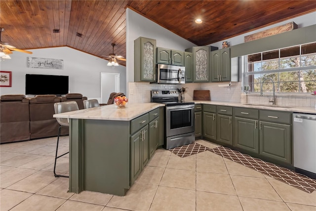 kitchen featuring light tile patterned floors, a peninsula, a sink, vaulted ceiling, and appliances with stainless steel finishes