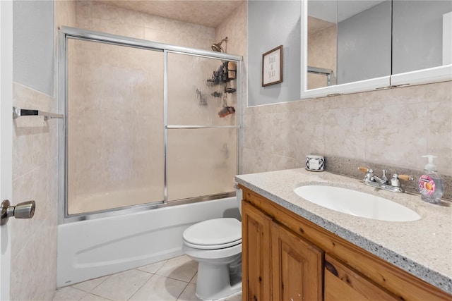 bathroom with tile patterned flooring, toilet, bath / shower combo with glass door, vanity, and tile walls