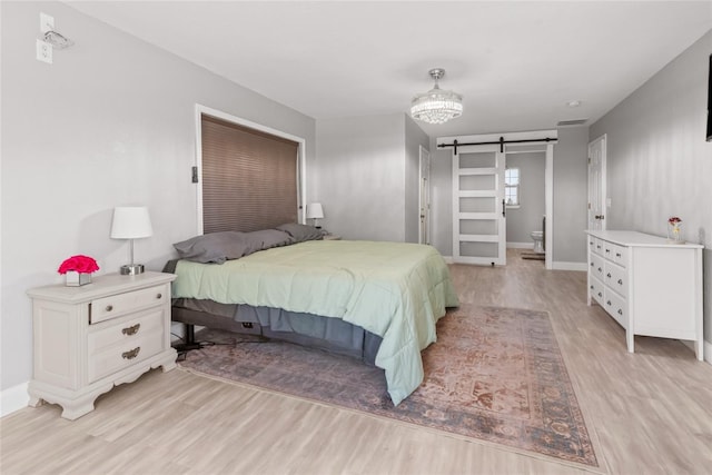 bedroom with baseboards, a barn door, visible vents, and light wood-style floors