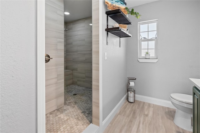 full bath with baseboards, a tile shower, wood finished floors, and vanity