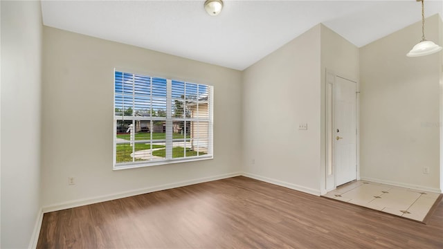 spare room featuring light wood finished floors, baseboards, and vaulted ceiling