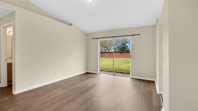 spare room featuring lofted ceiling, dark wood-style floors, and baseboards